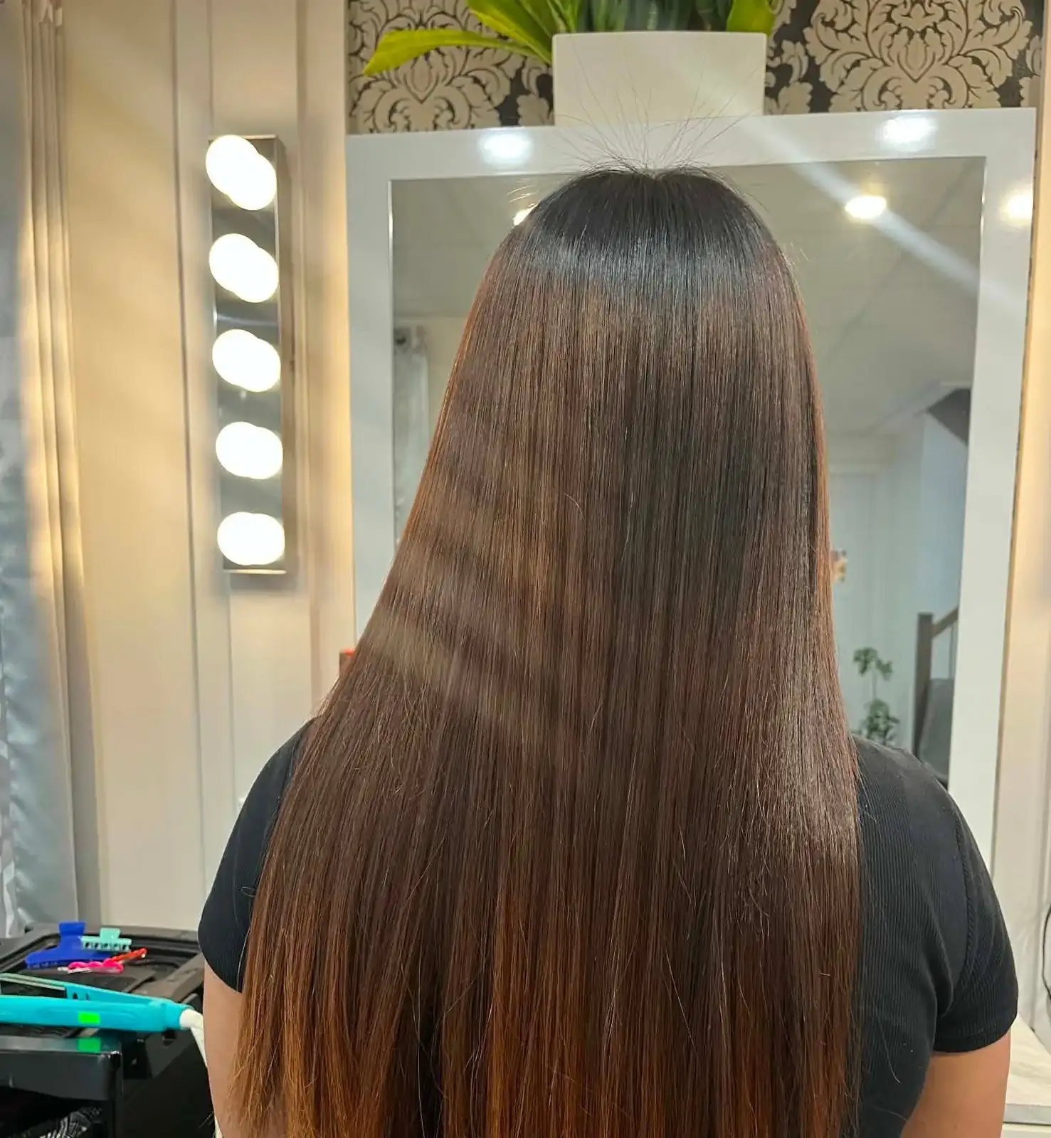 Longs cheveux bruns lissés, vus de dos, devant le miroir éclairé du salon