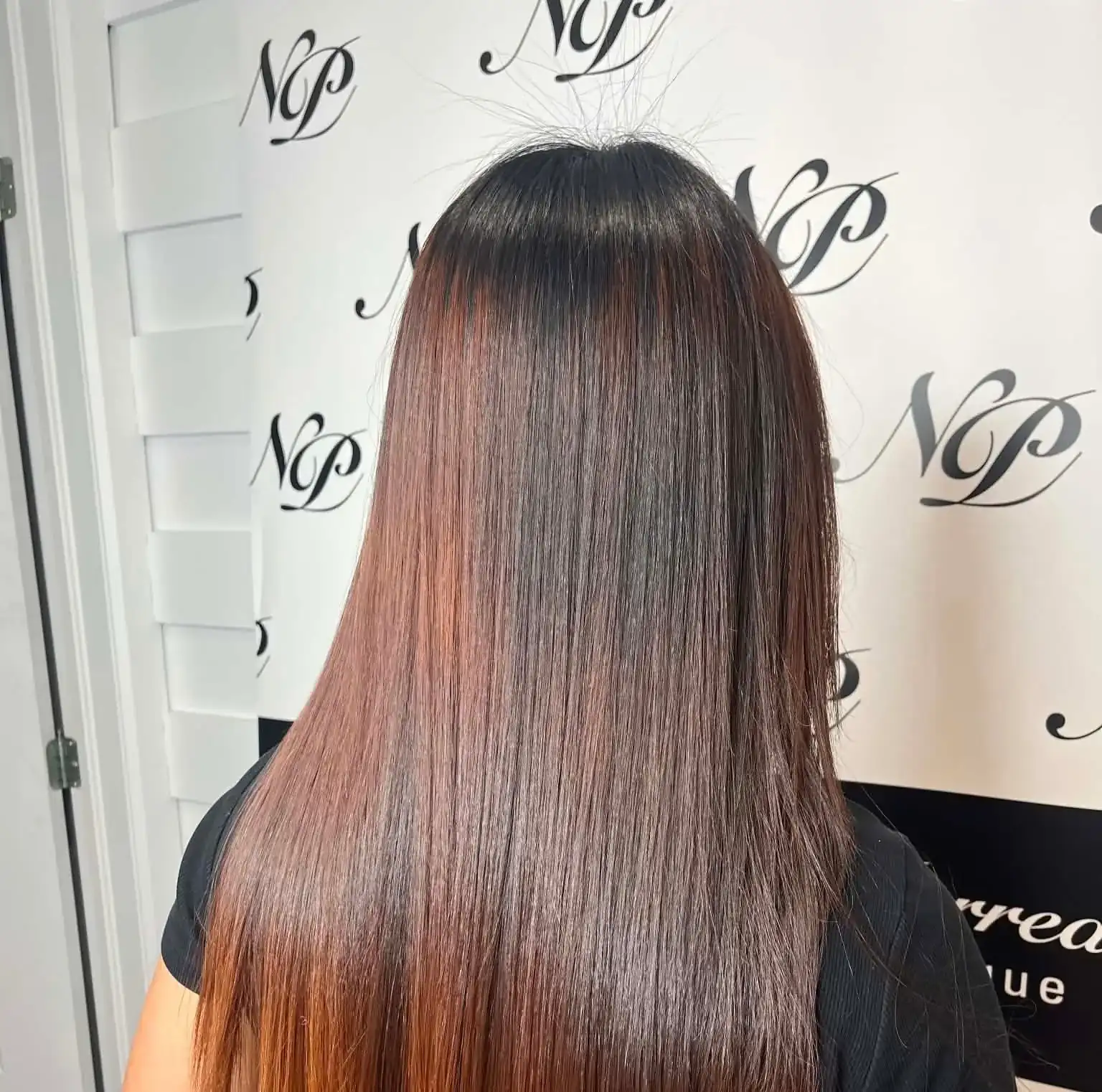 Longs cheveux aux reflets cuivrés, vus de dos, devant le mur au monogramme du salon