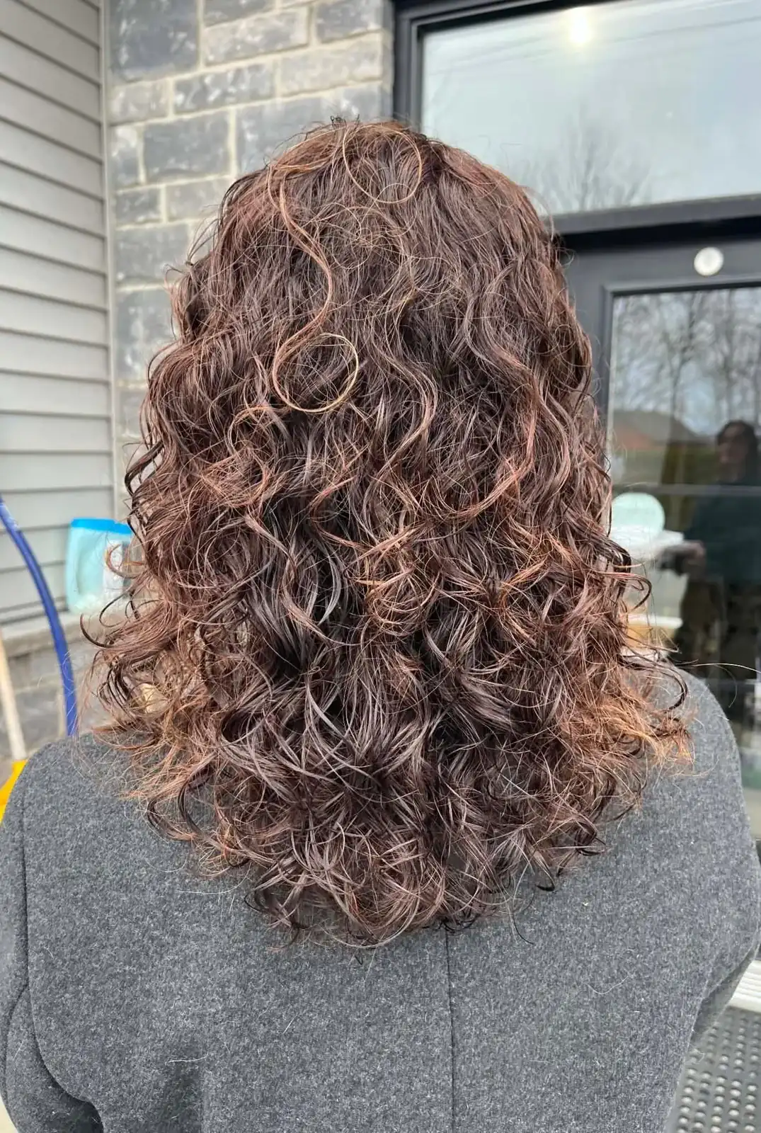 Boucles souples aux reflets cuivrés, vues de dos, à l’extérieur du salon