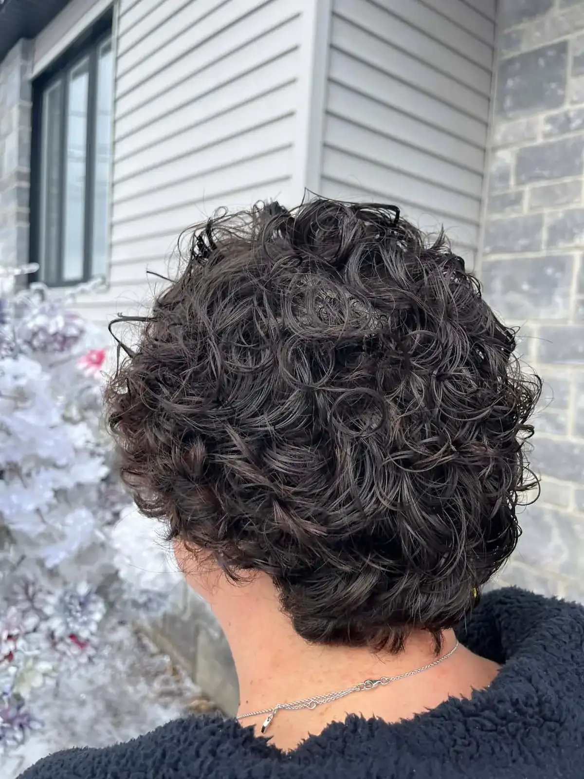 Boucles serrées sur cheveux courts foncés, vues de dos, devant la façade du salon